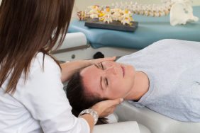 Woman lying on table while chiropractor massages neck